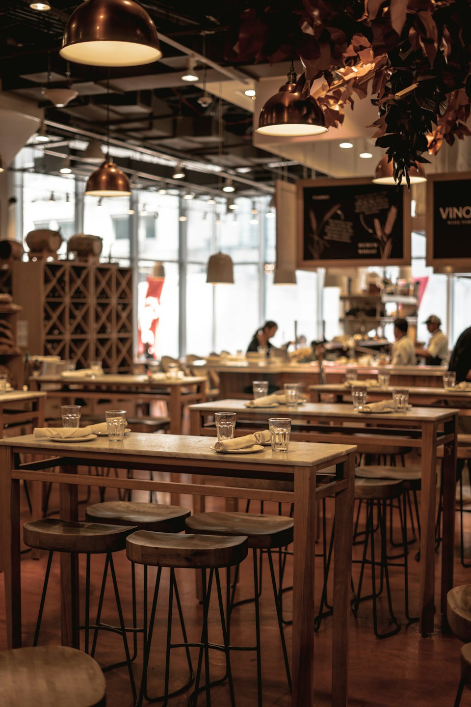 Jadalnia restauracyjna z drewnianymi stołami, marmurowymi blatami i stołkami barowymi.