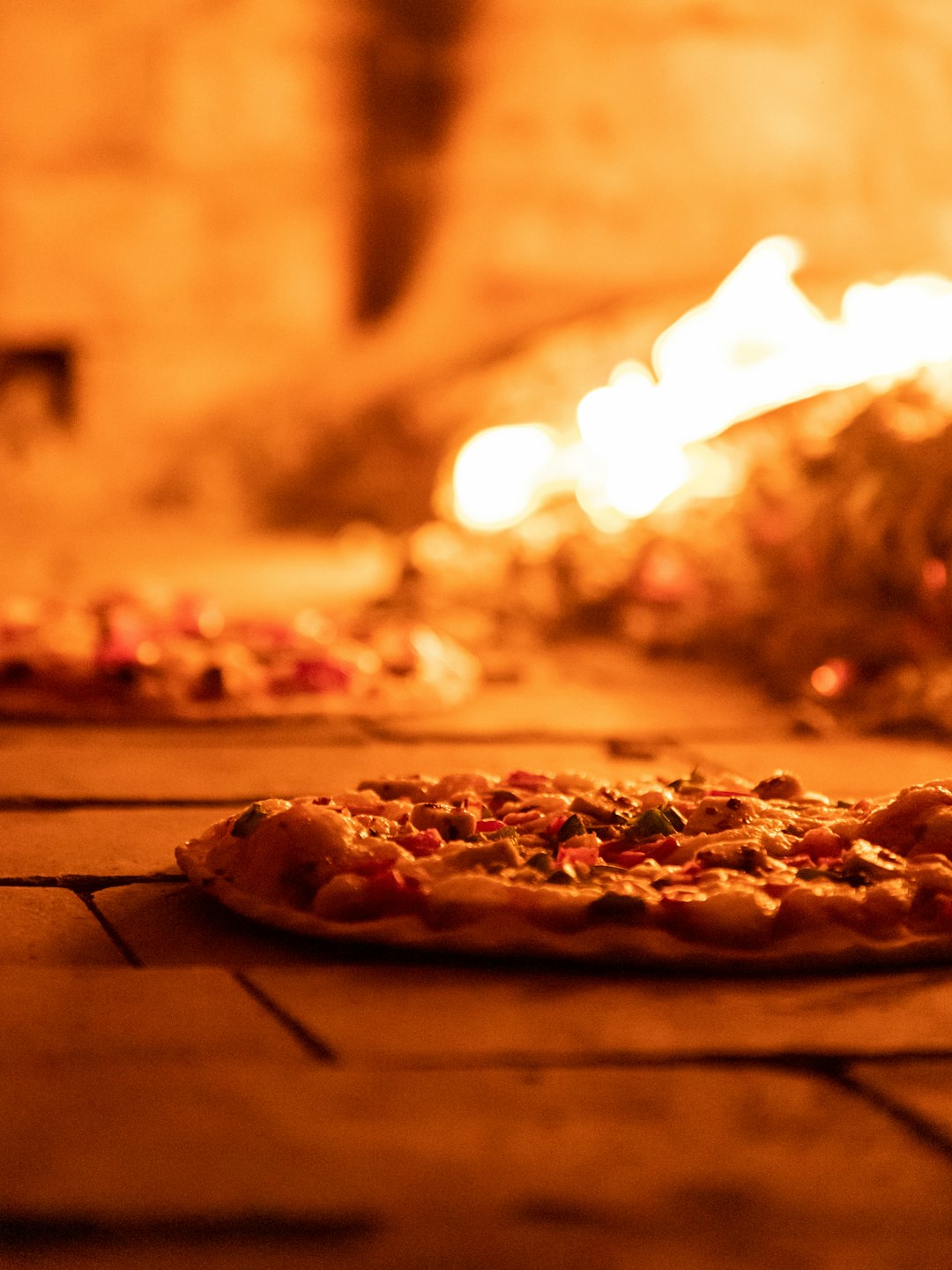 Pizza piekąca się w rozgrzanym piecu opalanym drewnem z kolorowymi dodatkami.